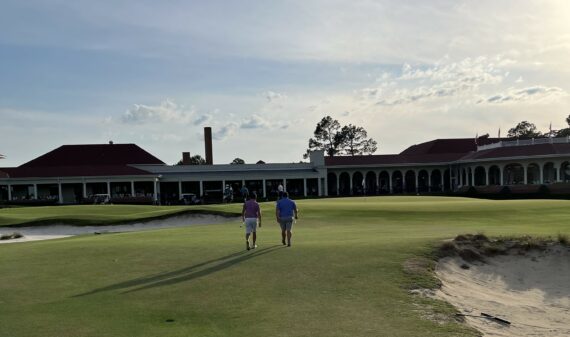 Gabe August and his playing partner walk up to the 18th green with putters in hand, the veranda awash in spectators.